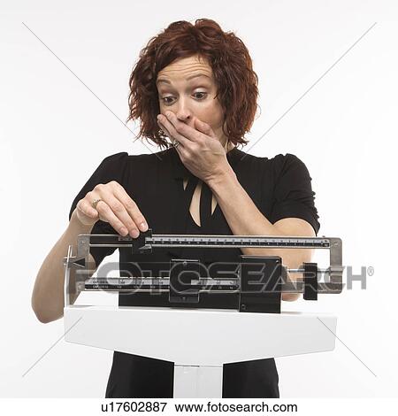 Stock Photo - Pregnant Caucasian mid-adult woman surprised by her weight shown on scale.. Fotosearch
