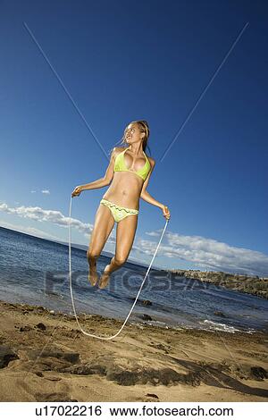 Stock Photograph - Young adult Asian Filipino female in bikini jumping rope on beach . Fotosearch