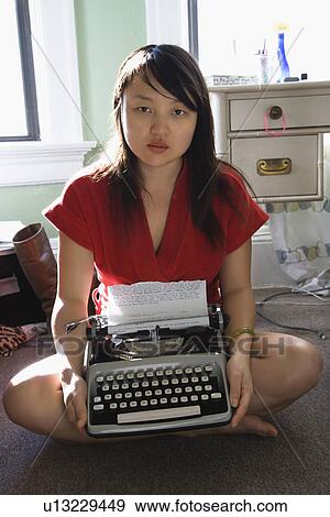 Stock Photo - Pretty Asian young woman sitting on floor in red robe holding typewriter.. Fotosearch
