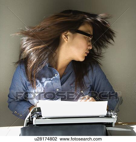 Stock Image - Pretty young woman sitting at typewriter swinging head and hair around. Fotosearch