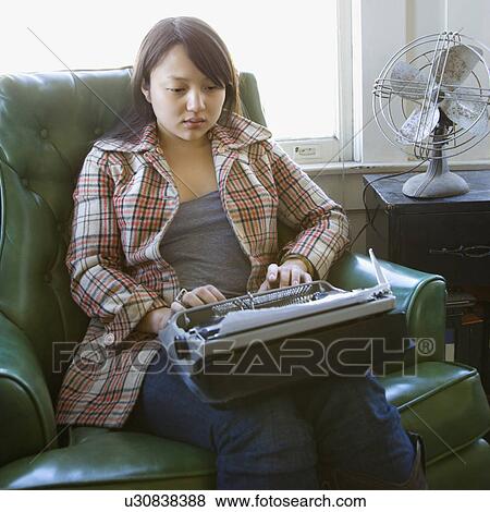 Stock Photo - Pretty young woman sitting in green chair typing on typewriter. Fotosearch