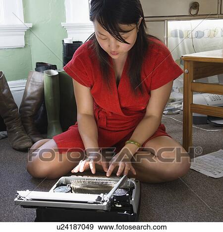 Stock Photo - Pretty young woman sitting on floor in red robe typing on typewriter. Fotosearch