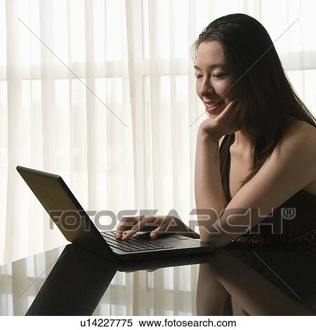 Stock Photography - Taiwanese mid adult woman on laptop smiling.. Fotosearch