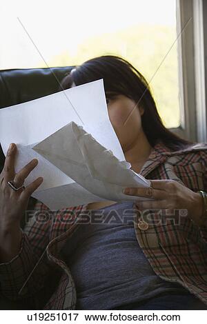 Stock Photo - Young Asian woman sitting in green chair reading letter.. Fotosearch