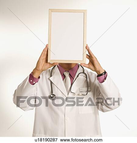 Stock Photo - Male doctor holding blank sign over face. Fotosearch
