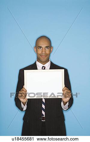 Stock Image - Man holding blank sign against blue background. Fotosearch
