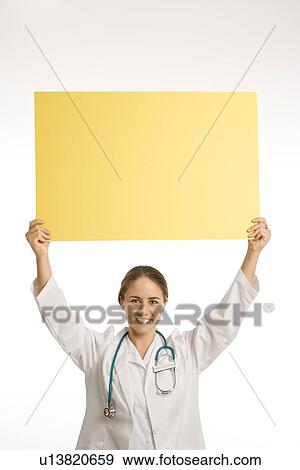 Portrait of doctor holding up blank yellow sign smiling and looking at viewer View Large Photo Image Stock Photo - Portrait of doctor holding up blank yellow sign smiling and looking at viewer. Fotosearch