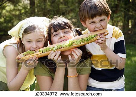 Stock Image - Three children sharing a large sandwich. Fotosearch