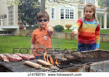 Stock Image - Boy and girl standing near a barbecue. Fotosearch