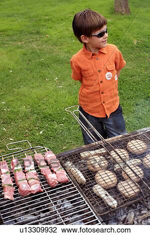 Stock Image - Boy standing near a barbecue. Fotosearch