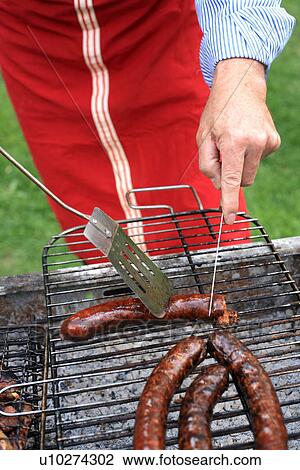 Stock Image - Mature man cooking food at a barbecue. Fotosearch