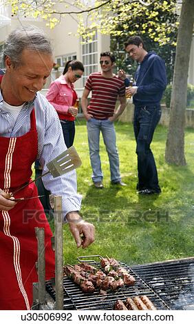 Stock Image - Mature man cooking food at a barbecue. Fotosearch