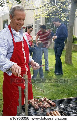 Mature man cooking food at a barbecue View Large Photo Image Stock Photograph - Mature man cooking food at a barbecue. Fotosearch
