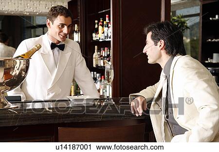 Stock Image - Man sitting at a bar talking to the bartender. Fotosearch