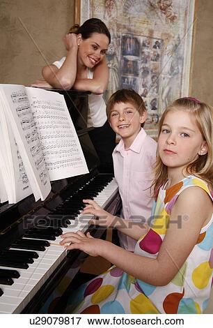 Stock Photo - Mother looking at her children playing piano. Fotosearch