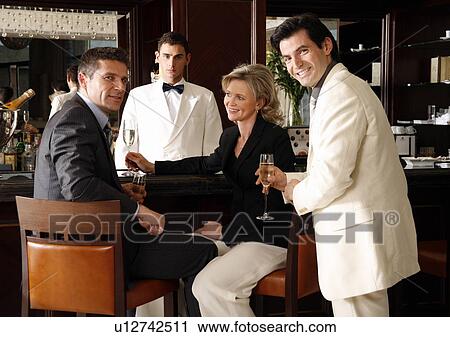 Stock Image - Two men and a woman sitting at a bar drinking. Fotosearch