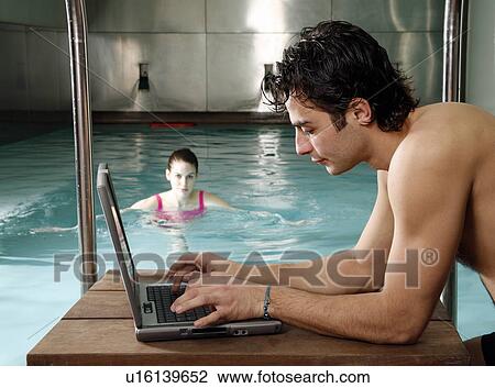 Stock Image - Man on computer nex t to a swimming pool. Fotosearch