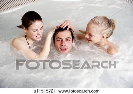 Stock Image - One man with two women in jacuzzi at a spa. Fotosearch