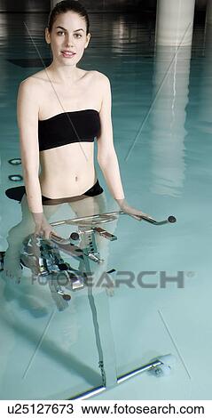 Stock Image - Young woman on exercise bike in spa pool. Fotosearch