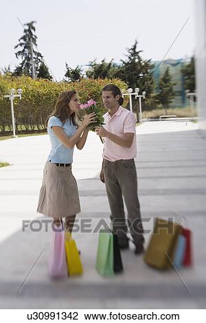 Stock Image - Couple with shopping bags, man offering roses. Fotosearch
