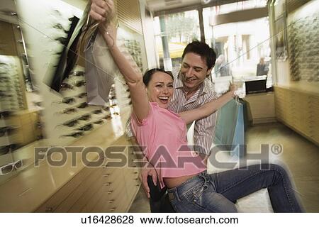 Stock Photo - Happy couple posing with shopping bags in a sunglasses store. Fotosearch