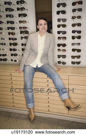Stock Image - Woman posing in front of sunglasses display. Fotosearch