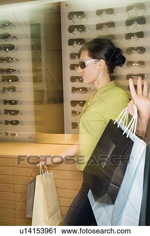 Stock Image - Woman shopping in sunglasses store. Fotosearch