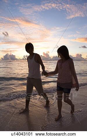 Stock Image - Young couple walking on beach, hand in hand, Saipan, USA . Fotosearch
