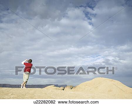 Stock Image - Man playing golf at rock strata. Fotosearch