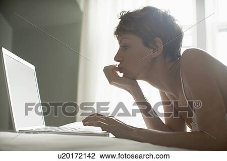 Mid adult woman using laptop on bed (low angle view) View Large Photo Image Stock Image - Mid adult woman using laptop on bed (low angle view). Fotosearch