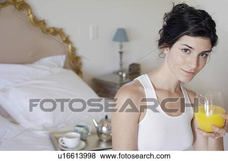 Stock Photo - Young woman drinking orange juice on bed (portrait). Fotosearch
