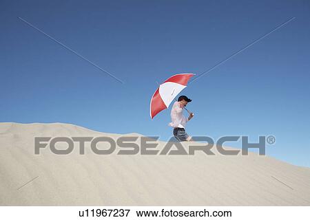 Young woman with umbrella walking on sand dune (low angle view) View Large Photo Image Stock Photo - Young woman with umbrella walking on sand dune (low angle view). Fotosearch