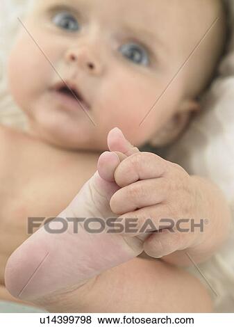 Stock Photo - Baby laying down holding foot. Fotosearch