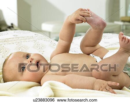 Stock Photograph - Baby laying down holding foot. Fotosearch