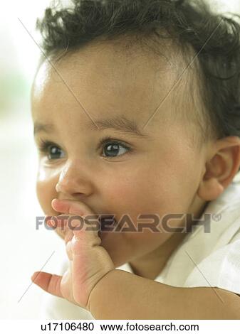 Stock Image - Baby's face close up with hand by mouth. Fotosearch