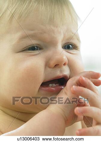 Stock Image - Baby's face close up with hands by mouth. Fotosearch