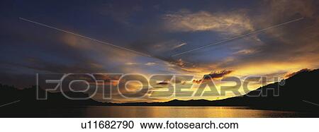 Stock Image - Landscape view with body of water at dusk. Fotosearch