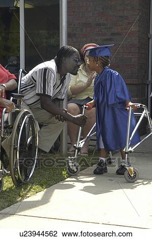 A precious moment between a father and his daughter, who has disabilities and utilizes a walker for mobility assistance, as she prepares to participate in her preschool graduation. View Large Photo Image Stock Image - A precious moment between a father and his daughter, who has disabilities and utilizes a walker for mobility assistance, as she prepares to participate in her preschool graduation.. Fotosearch