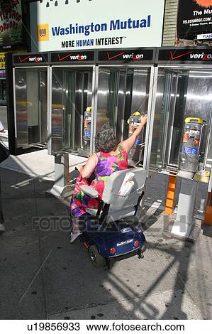 Stock Image - A woman trying to use non accessible pay phones.. Fotosearch
