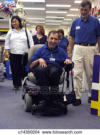 Picture - Man with a disability, utilizing a scooter/cart for mobility, checking out a retail establishment.. Fotosearch