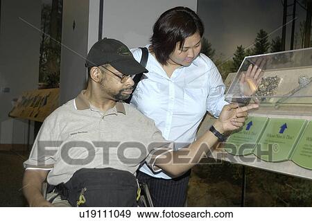 Man with a disability, utilizing a wheelchair for mobility, visiting an exhibit with a friend. View Large Photo Image Stock Photo - Man with a disability, utilizing a wheelchair for mobility, visiting an exhibit with a friend.. Fotosearch