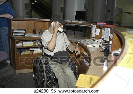 Stock Photography - Man with a disability working as a receptionist answering phones at a museum.. Fotosearch