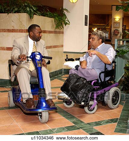 Two men with disabilities, both utilizing scooter/wheelchair for mobility, talking while on break during a conference. View Large Photo Image Stock Photograph - Two men with disabilities, both utilizing scooter/wheelchair for mobility, talking while on break during a conference.. Fotosearch