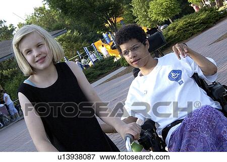Stock Photo - Woman, using a wheel chair for mobility, at the park with a friend.. Fotosearch