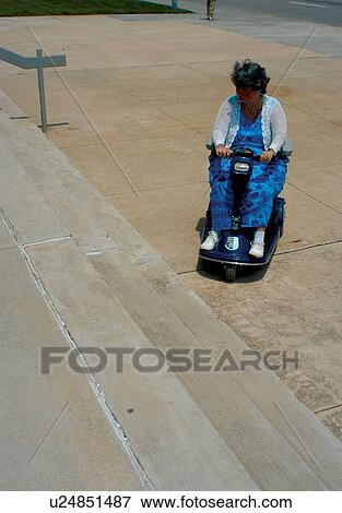 Woman with a physical disability utilizing a power scooter/cart for mobility encountering barriers in large city. View Large Photo Image Stock Photo - Woman with a physical disability utilizing a power scooter/cart for mobility encountering barriers in large city.. Fotosearch