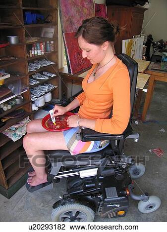 Stock Image - Young artist (female wheelchair user) mixes paint in her studio.. Fotosearch