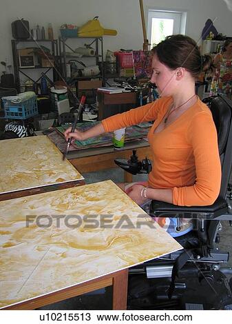 Stock Image - Young woman (electric wheelchair user) paints on canvas in her studio.. Fotosearch