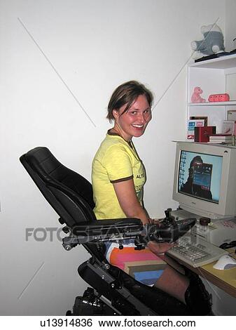 Young woman smiles at camera while using electric wheelchair to access a computer workstation. View Large Photo Image Stock Photograph - Young woman smiles at camera while using electric wheelchair to access a computer workstation.. Fotosearch