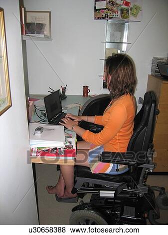 Stock Photo - Young woman uses electric wheelchair to access a computer workstation.. Fotosearch