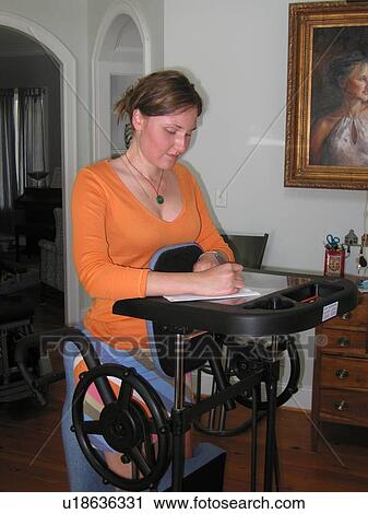 Stock Image - Young woman uses specialized stander to work in her home while stretching her tendons.. Fotosearch